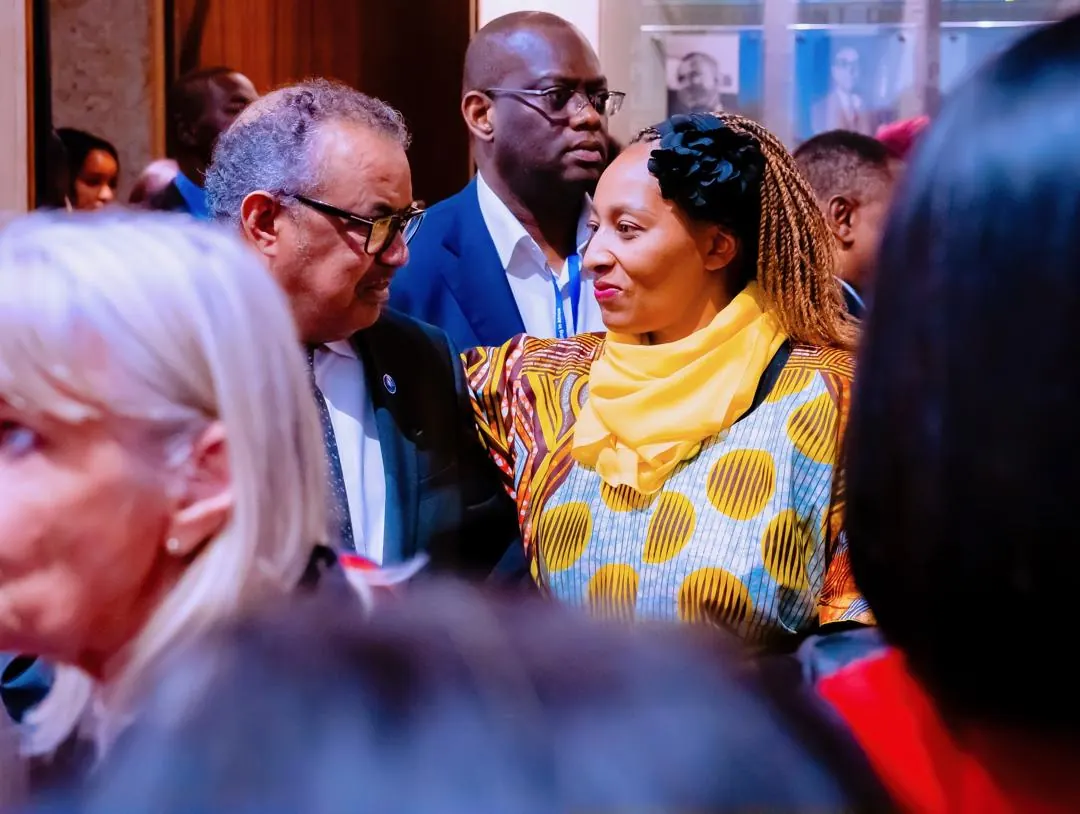 A woman in a yellow scarf and patterned dress listening to a man in glasses during a conversation at an event