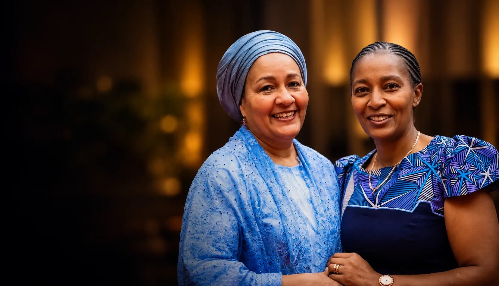 Two women in blue attire smiling and standing side by side